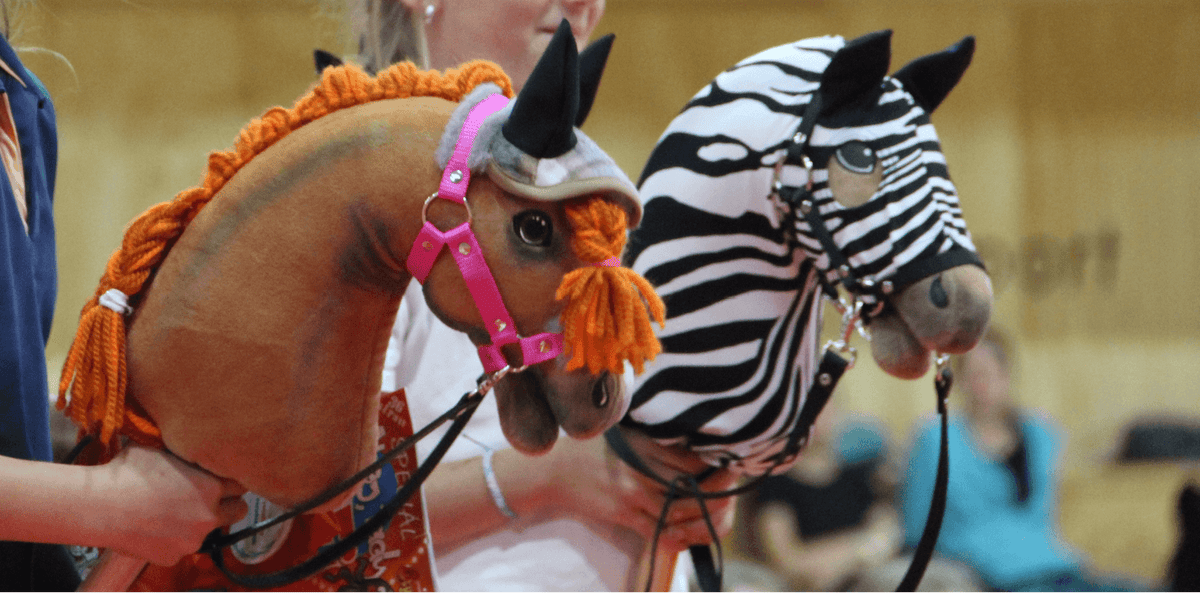 Zwei Hobby Horses mit geflochtenen Mähnen, eines braun mit orangem Garn und eines mit Zebramuster