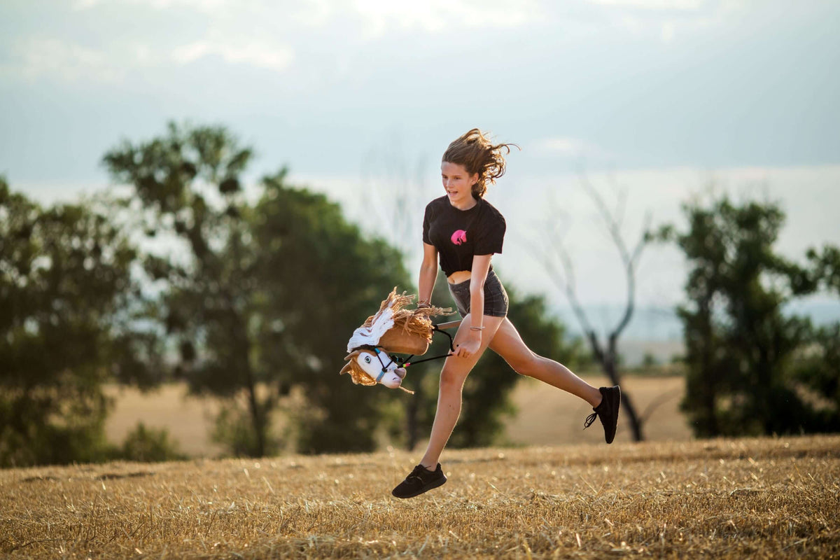 Junges Mädchen springt beim Hobby-Horsing-Training im Freien mit einem Hobby Horse