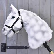 Hobby Horse Elektra mit Schwarzem Halfter von Hobby Horse LarDen mit plüschigem weißem Design, blauen Augen und schwarzem Halfter, auf einem Stab montiert, vor einer grauen Holzwand.