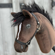 Nahaufnahme von Hobby Horse Lucas mit schwarzem Halfter von Hobby Horse LarDen, ein brauner Hannoveraner-Hengst als Hobby Horse mit schwarzer Mähne, weißer Blesse und schwarzem Halfter, vor unscharfem Holzhintergrund.