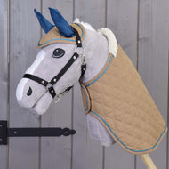 Das Hobby Horse LarDen Set Almond Star zeigt ein Plüsch-Hobby Horse mit beigefarbener gesteppter Decke, blauer Fliegenhaube, weißer Mähne und schwarzem Zaumzeug auf einem Holzstab vor einer grauen Holzwand.