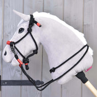 Ein grauer Plüsch-Hobby-Horse-Kopf mit schwarzer Trense, roten Akzenten und dem Hobby Horse LarDen Seilset Spark ist an einem Holzstab befestigt und vor einem Hintergrund aus hellen Holzpaneelen zu sehen.