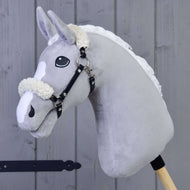 Hobby Horse LarDen Schwarzes Halfter mit Fell - Kunstleder an einem grauen Plüschpferd mit weißer Mähne und Holzstab, vor einer Holzpaneelwand.