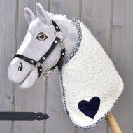 Decke Cube Blue von Hobby Horse LarDen ist ein plüschiges Hobby Horse mit grauem Gesicht, schwarzem Zaumzeug und einer Decke mit blauen Akzenten, auf einem Holzstab vor Holz-Hintergrund.