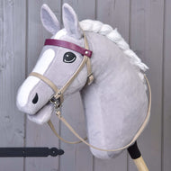 Ensemble similicuir Bordeaux - bride, rênes et martingale de Hobby Horse LarDen, sur un Hobby Horse gris avec crinière blanche, œil noir, bandeau frontal violet et visage de style cartoon, debout devant un fond en bois.