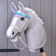 Hobby Horse LarDen mit grauem Plüsch-Hobby Horse mit ausdrucksstarken Augen, weißer Mähne und Kunstlederset Aqua - Zaumzeug, Zügel und Martingale auf einem Holzstab vor hellgrauem Hintergrund aus Holzpaneelen.