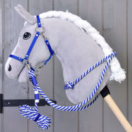 Ein graues Plüsch-Hobby Horse von Hobby Horse LarDen mit Set Start Blau (Halter, Halsring, Führstrick, Zügel), mit blau-weißem Führstrick an einem Holzstab, steht vor einer grauen Holzwand.