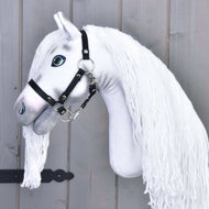 Hobby Horse Quicksilver mit Schwarzem Halfter von Hobby Horse LarDen mit weißem Körper, schwarzem Halfter, blauen Augen und einer aufgestickten Träne unter einem Auge vor einer grauen Holzwand.