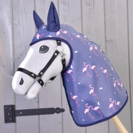 Eine Hobby Horse LarDen Regendecke Flamingo: ein graues Hobby Horse mit marineblauer Regenkapuze mit rosa Flamingos, vor einer Holzwand mit schwarzem Metallscharnier platziert.