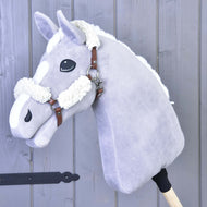 Braunes Halfter Full Fell - Kunstleder von Hobby Horse LarDen an einem plüschigen hellgrauen Hobby Horse mit weißer Mähne und Abzeichen, auf einem Holzstab und fotografiert vor grauem Holzpaneel-Hintergrund.
