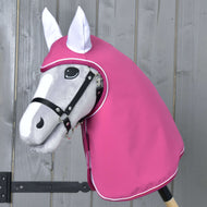 Regendecke Larden von Hobby Horse LarDen, ein graues Hobby Horse mit schwarzem Zaumzeug und rosafarbener Kapuze als Wetterschutz, ist vor einer Holzwand zu sehen.