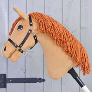 Hobby Horse Little Angel mit Schwarzem Halfter von Hobby Horse LarDen mit weißen Akzenten und orangefarbener Garnmähne, auf einem Stock vor hellgrauem Holzbackground.