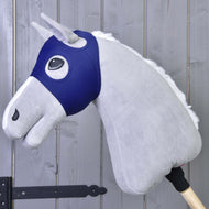 Masque de cheval sans oreilles LarDen de Hobby Horse LarDen sur un Hobby Horse gris avec crinière blanche et manche en bois, contre un mur en bois avec charnières visibles.
