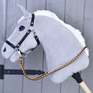 Hobby Horse gris de Hobby Horse LarDen avec crinière blanche, bride noire et rênes Pomello tricotées, rênes en corde de polypropylène tressée orange et marron, monté sur un bâton en bois devant un fond en bois gris.