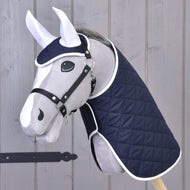 Set Monte von Hobby Horse LarDen zeigt einen grauen Plüschkopf eines Hobby Horse mit einer dunkelblauen gesteppten Decke und passendem Fliegenhauben-Set mit weißer Einfassung, auf einem Stock vor hellem Holz – ideal als dekoratives Stück.