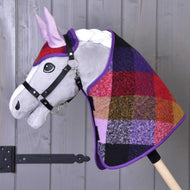 L’Ensemble Automne à Carreaux 2 de Hobby Horse LarDen présente un Hobby Horse en peluche au visage gris avec bride noire et encolure colorée en patchwork à carreaux, monté sur un bâton en bois, sur fond de mur en bois.