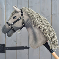 Hobby Horse Swing mit schwarzem Halfter, Größe S von Hobby Horse LarDen, inspiriert von der Eleganz eines Hannoveraner-Hengstes, mit grauer Garnmähne, schwarzem Zaumzeug und Knopfaugen, auf einem Holzstab montiert vor grauem Holzhintergrund