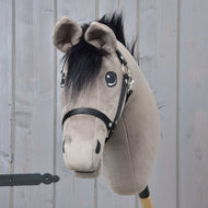 Hobby Horse Thor mit Schwarzem Halfter von Hobby Horse LarDen mit weichem grauem Kopf, schwarzer Mähne und Geschirr auf einem Holzstab vor einem Hintergrund aus hellen Holzpaneelen.