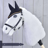 Ein graues Hobby Horse LarDen mit schwarzen Zügeln und weißer Mähne trägt die Ohrenkappe gehäkelt Black Gold zum Insektenschutz und zeigt schwarze Gesichtsdetails, vor hellem Holzhintergrund.