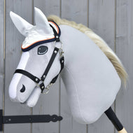 Das Hobby Horse LarDen Ohrenkappe Speedy ist ein realistisches graues Hobby Horse mit schwarzem Zaumzeug, weißer Mähne und weißer fliegenschützender Ohrenkappe, auf einem Holzstab vor einer hellgrauen Holzwand.