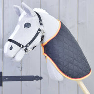 Die Decke Flag von Hobby Horse LarDen an einem grauen Hobby Horse mit schwarzem Zaumzeug und gesteppter Decke mit orangefarbener Einfassung, montiert auf einem Holzstab vor einem grauen Holzzaun.