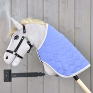 Graues Hobby Horse mit schwarzem Zaumzeug und Decke Light Violett von Hobby Horse LarDen auf einem Stock, vor einer hellen Holzwand.