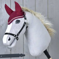 Die Hobby Horse LarDen Ohrenkappe gehäkelt Lux Maroon ist auf einem Plüsch-Steckenpferd mit weißem Gesicht, schwarzem Zaumzeug, flauschiger blonder Mähne, bordeauxfarbenen Stoffohren und passender Ohrenkappe vor grauem Holzhintergrund zu sehen.