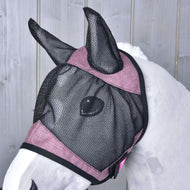 Ein weißes Pferd trägt die Hobby Horse LarDen Fliegenmaske de Luxe Pink, eine waschbare schwarze und rosa Mesh-Maske, die Ohren und Gesicht bedeckt, vor hellgrauem Holz-Hintergrund.