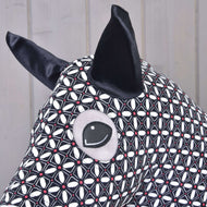 Nahaufnahme des Hobby Horse LarDen Hobby Horse Schutzanzug DeLuxe (Lycra) mit waschbarem schwarzem und weißem geometrischem Lycra-Stoff, großen schwarzen Ohren und gesticktem Auge vor hellem Holz-Hintergrund.