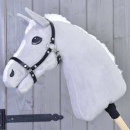 Ein graues Plüsch-Hobby Horse von Hobby Horse LarDen mit weißer Mähne und Halfter - schwarzes Kunstleder, auf einem Holzstab montiert vor einer Holzpaneelwand.