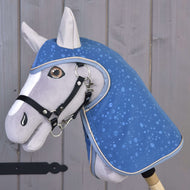The Raincoat Dolly (softshell) by Hobby Horse LarDen features a gray hobby horse with a blue, water drop-patterned blanket and bridle on a wooden stick—perfect for all-weather play against a rustic wooden plank backdrop.