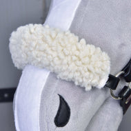 Nahaufnahme von Set Harmony Elsa von Hobby Horse LarDen mit weißem, lockigem Plüsch-Nasenriemen, schwarzem Zaumzeug aus Kunstleder und gesticktem schwarzem Nüstern auf weichem grauem und weißem Stoff.