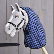 Ein graues Plüsch-Hobby Horse mit schwarzem Zaumzeug und der Stalldecke Blue von Hobby Horse LarDen mit blau-schwarzem Hahnentrittmuster ist auf einem Holzstab montiert und vor einer Wand aus Holzplanken positioniert.