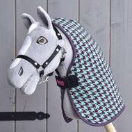 Ein handgefertigtes graues Hobby Horse mit schwarzem Zaumzeug, bekleidet mit der „Stalldecke Green“ von Hobby Horse LarDen, ist vor einem Holz-Hintergrund dargestellt.