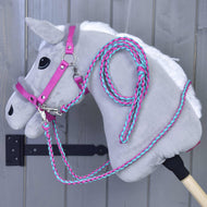 The Hobby Horse LarDen Set Perfect Combination Pink, a gray plush hobby horse with pink and turquoise fur-padded halter and reins, hangs on a wall-mounted hook against a gray wooden background.