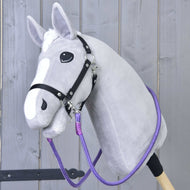 Rênes Viola de Hobby Horse LarDen sur un Hobby Horse gris avec liste blanche, bride noire et rênes faites main colorées, avec tête en peluche sur bâton solide, présenté devant une clôture en bois clair.