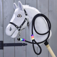 Hobby Horse - Longe arc-en-ciel de Hobby Horse LarDen, Hobby Horse gris avec crinière blanche, bride noire, rênes et longe à ruban arc-en-ciel autour du cou, présenté devant un panneau en bois.