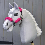 Hobby Horse LarDen mit einem handgefertigten grauen Hobby Horse mit weißer Mähne und weißer Gesichtszeichnung, das Schwarzes Halfter mit Full rosa Fell - Kunstleder trägt, vor einem Holzhintergrund.