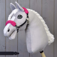 Hobby Horse LarDen Schwarzes Halfter mit rosa Fell - Kunstleder mit hellgrauem Plüschkopf, rosa Fellakzenten, weißer Garnmähne und schwarzem Halfter auf einem Holzstab vor einem Hintergrund aus Holzplanken.