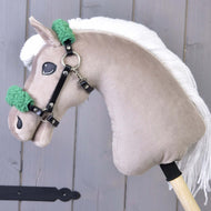 Ein Spielzeug von Hobby Horse LarDen mit beigem Plüschkopf, weißer Garnmähne und Schwarzes Halfter mit grünem Fell - Kunstleder vor grauem Holz-Hintergrund.