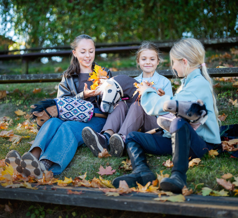 Tři dívky s Hobby Horse na podzimních schodech plných listí
