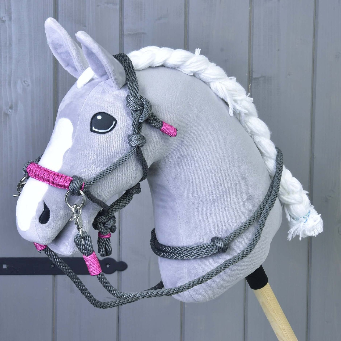 Ein plüschiges grauweißes Hobby Horse mit geflochtener Mähne und schwarzen Augen präsentiert das Hobby Horse LarDen Seilset Grau (Gr. M) vor einer Holzvertäfelung und hebt das einzigartige handgefertigte Reitzubehör hervor.