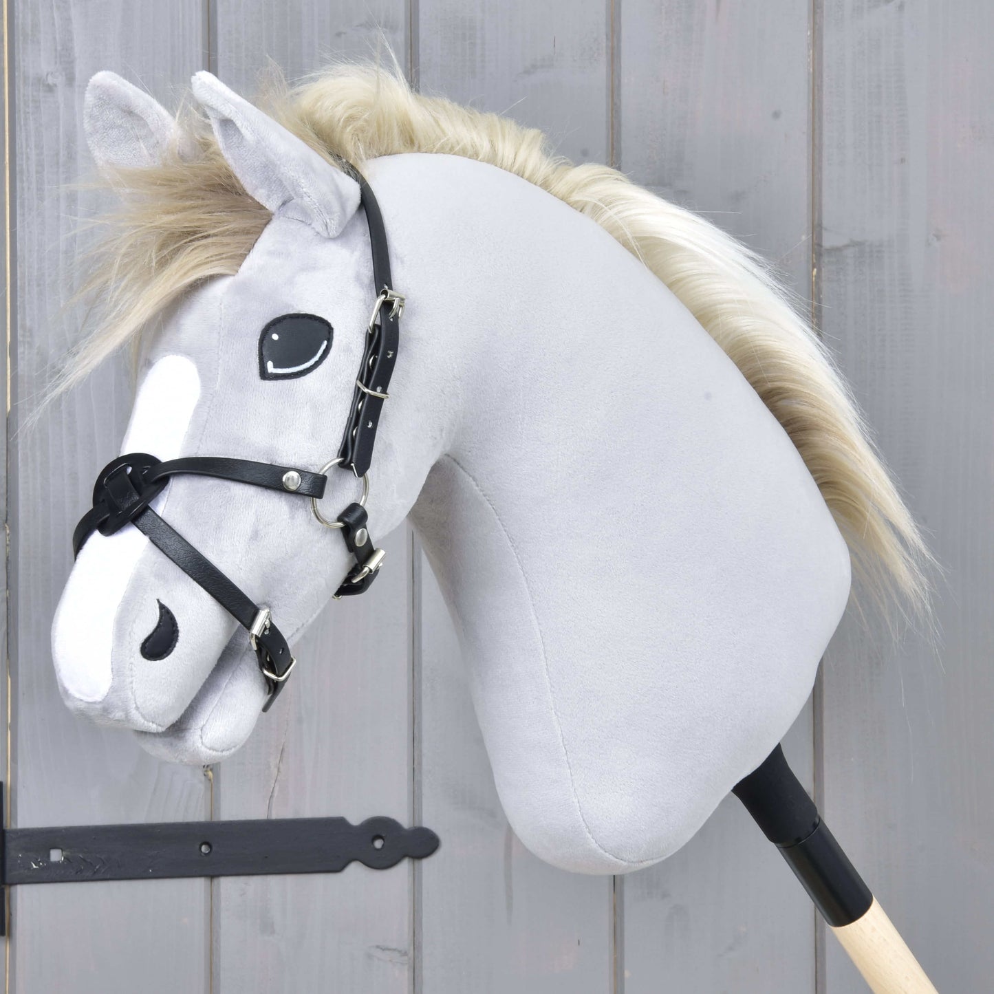 Das Hobby Horse LarDen „Reithalfter Mexico Schwarz“ ist ein graues Plüsch-Hobby Horse mit schwarzem Zaumzeug, Reithalfter aus Kunstleder und heller Mähne auf einem Stab, gezeigt vor einer grauen Holzwand.
