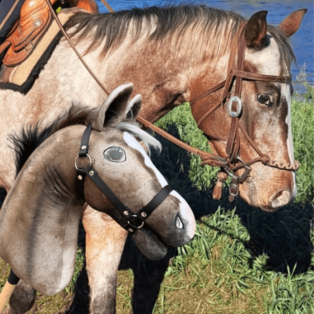 Une personne tient une marionnette « Hobby Horse personnalisé d'après votre photo » de Hobby Horse LarDen, modelée d’après un vrai cheval portant une bride, devant le cheval assorti debout sur l’herbe près de l’eau.