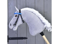 A gray hobby horse by Hobby Horse LarDen, featuring a Bridle with Blue Headband (size S) and white yarn mane, is mounted on a wooden stick and positioned against a gray wooden door.