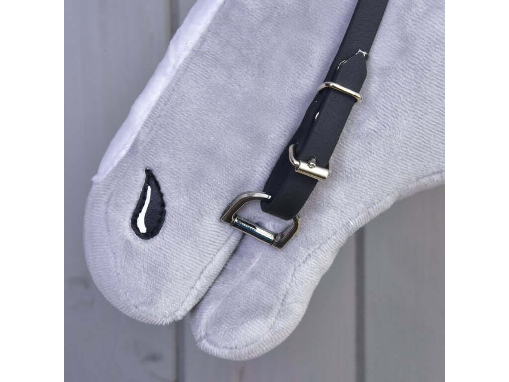A close-up of a Hobby Horse LarDen Bridle with Blue Headband (size S) on plush grey fabric shaped like a horse’s face, featuring a metal buckle and simple black and white embroidered eye against light-colored wood panels.