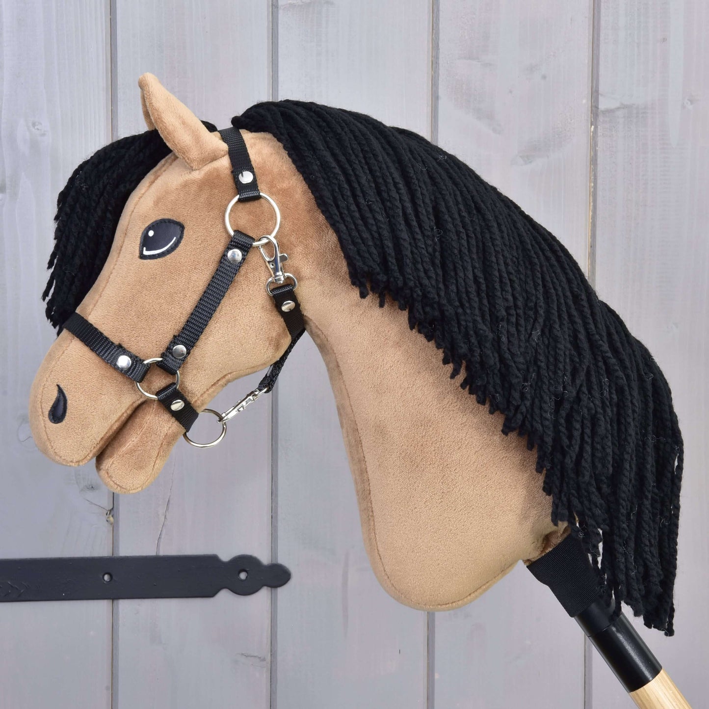 Hobby Horse Samantha mit Schwarzem Halfter von Hobby Horse LarDen mit beigefarbenem Gesicht, schwarzer Garnmähne, gestickten Details und schwarzem Halfter, präsentiert auf hellem Holzuntergrund.