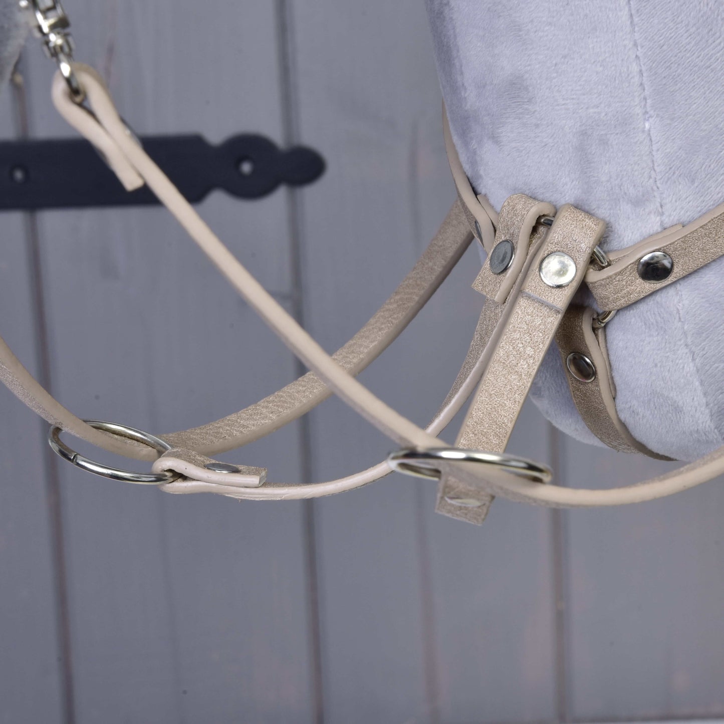 Close-up of the Bordeaux leatherette set—bridle, reins, and martingale—from Hobby Horse LarDen, featuring metal rings on a grey plush hobby horse head against a wooden background with a black decorative hinge.