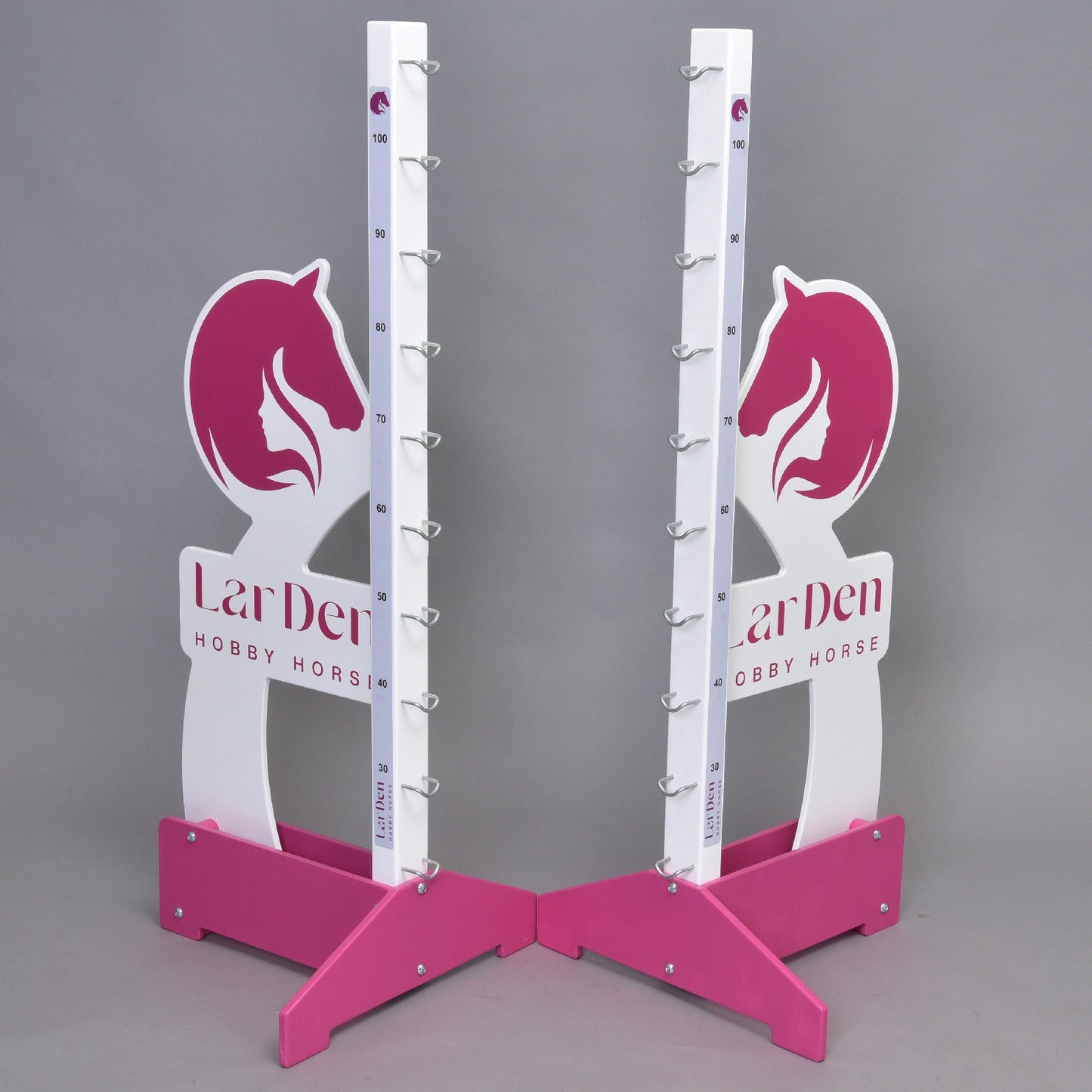 Deux montants LarDen jump 110 cm / 43 inch roses et blancs de Hobby Horse LarDen avec motifs de tête de cheval, repères de hauteur réglables et supports métalliques pour barre, sur fond gris. « LarDen HOBBY HORSE » est imprimé sur la base.