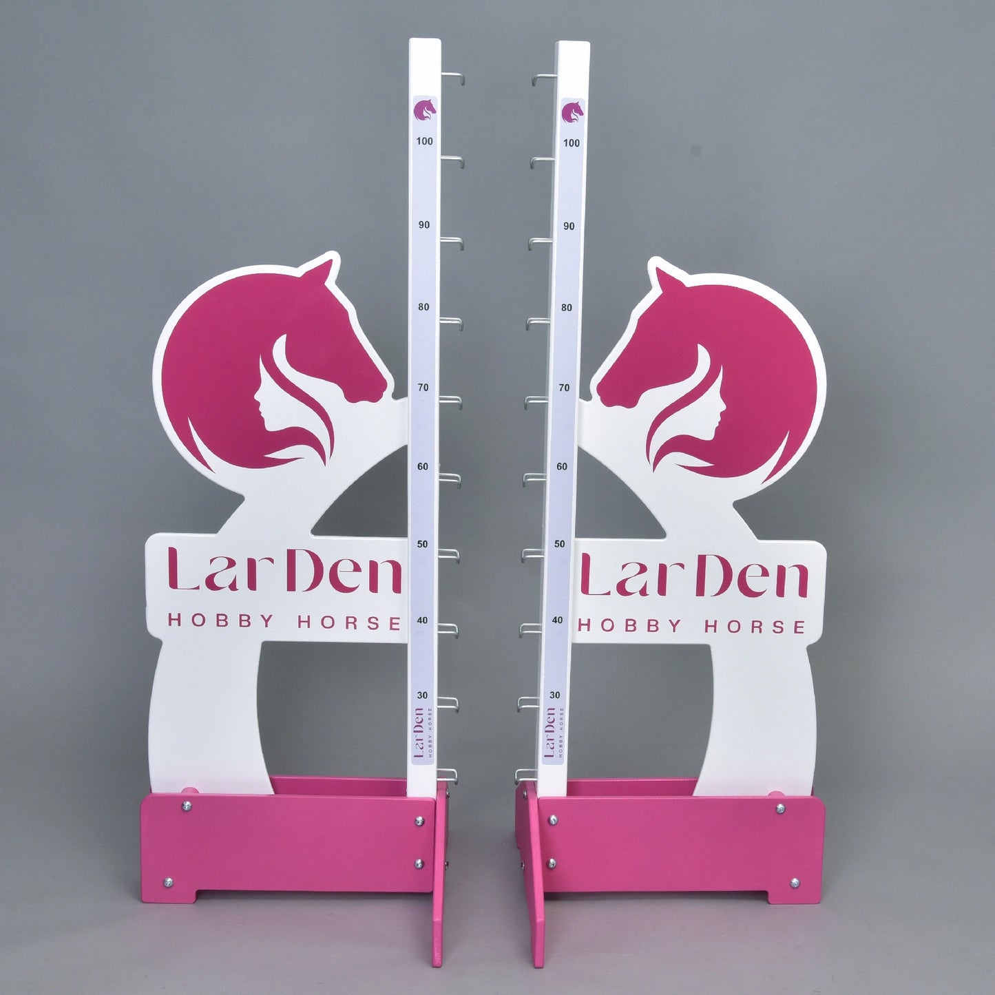 Deux montants LarDen jump 110 cm / 43 inch blancs et roses de Hobby Horse LarDen, avec hauteur réglable jusqu’à 110 cm, graphismes de tête de cheval et texte de la marque sur la base, parfaits pour monter à Hobby Horse, présentés sur fond gris uni.